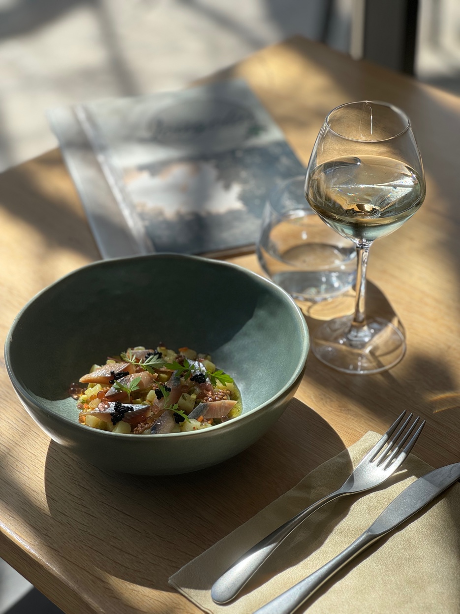 Bol en céramique verte de poisson mariné, pommes de terre et œufs de poisson, avec un verre de vin blanc sur une table en bois ensoleillée